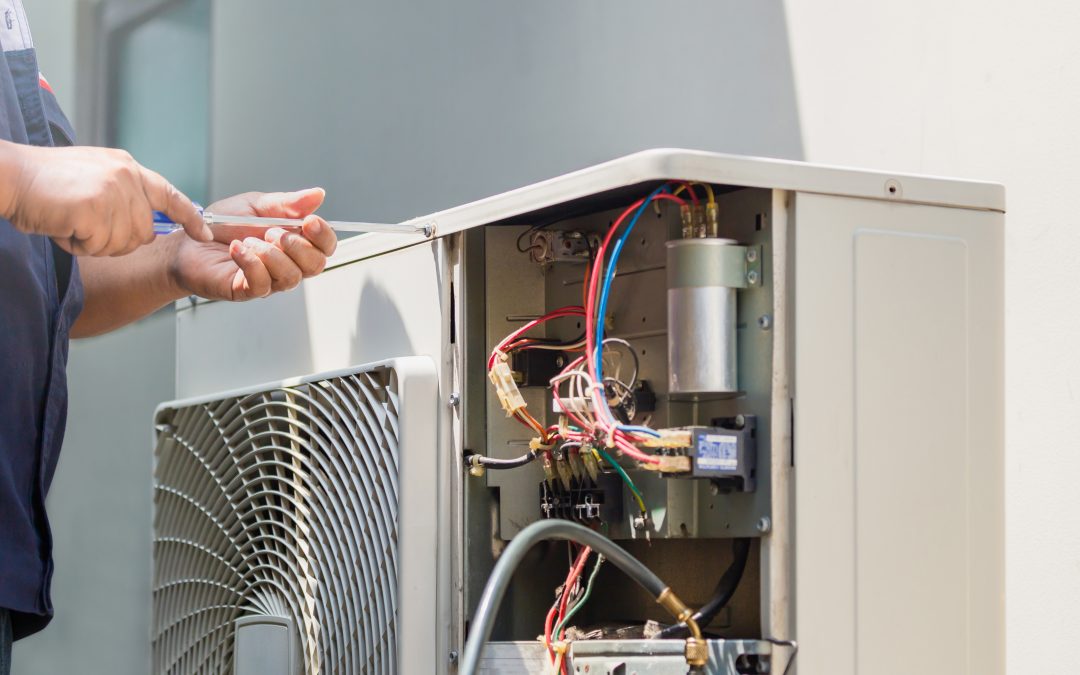 A technician working on the electrical components of an outdoor air conditioning unit using a screwdriver. AC Repair