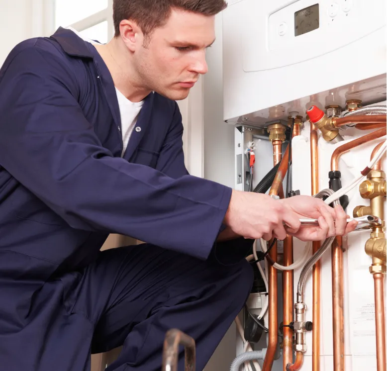 Boiler Services Near Me: A plumber in blue coveralls repairs pipes under a boiler system using a wrench.