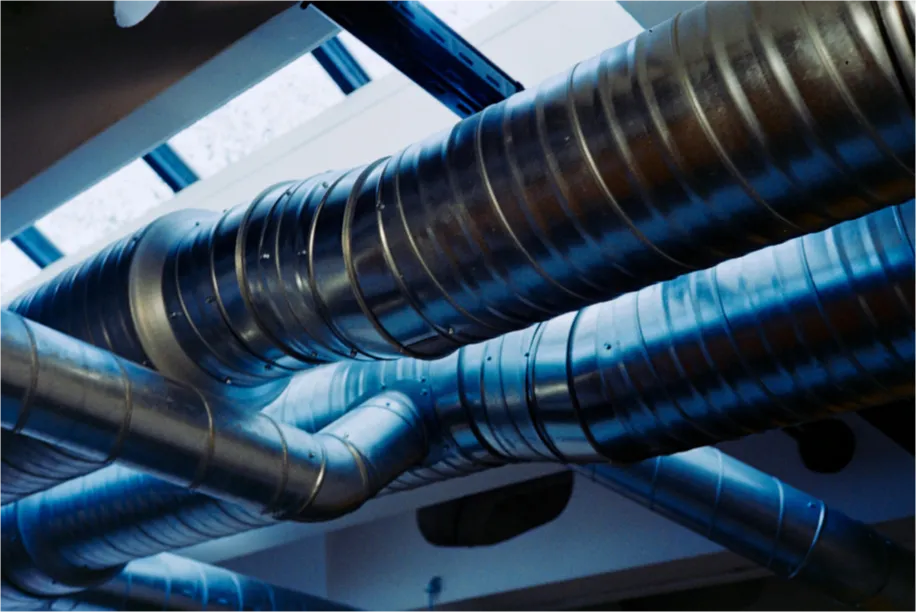 Metal air ducts run across a ceiling near skylights, illuminated by natural light.