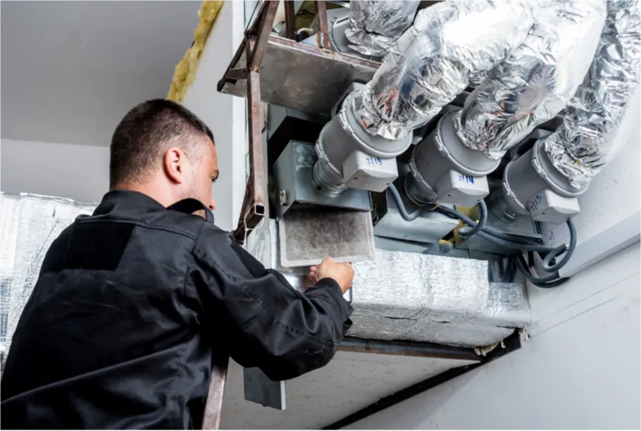 Technician in black overalls inspects and repairs ductwork and ventilation system on a ceiling.