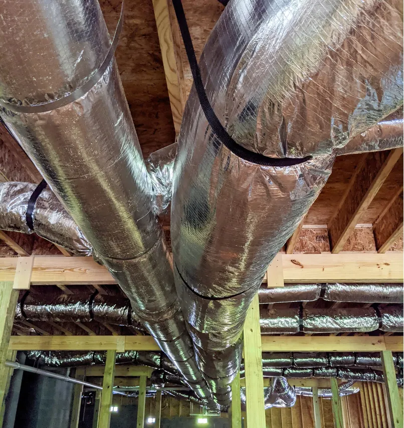 Silver insulated HVAC ducts suspended from a wooden ceiling in a building under construction.