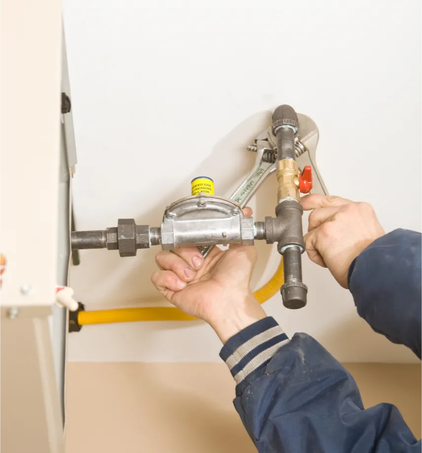 Person tightening a gas pipe connection to an appliance using a large adjustable wrench.