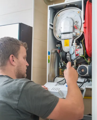 furnace-why Man repairing or servicing an open boiler or heating system, using tools and inspecting internal components.