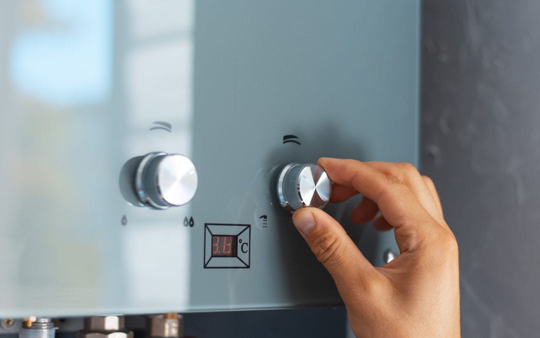 Hand adjusting the temperature knob on a modern tankless water heater mounted on a wall.