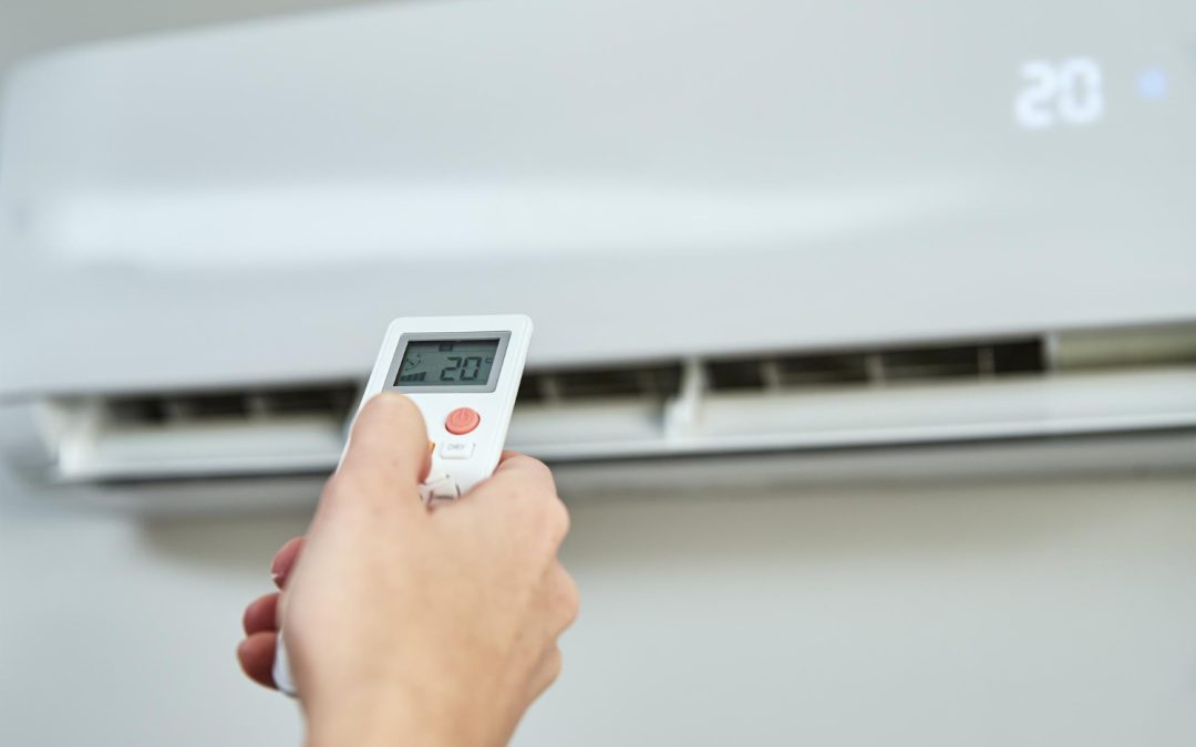 A hand holds a remote, setting an air conditioner to 20 degrees Celsius.